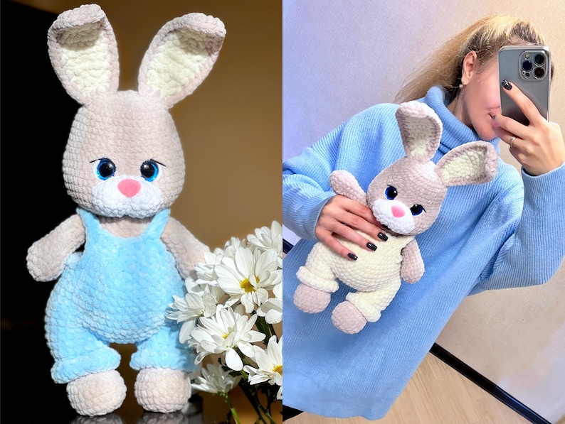 May include: A crocheted bunny plush toy with blue overalls. The bunny has a light brown body, white ears, and blue eyes. The bunny is sitting on a white surface with a bouquet of white flowers.