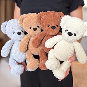 Puede incluir: Cuatro osos de peluche hechos a mano en varios colores: azul claro, beige, marrón y blanco. Cada oso tiene una nariz y ojos negros y está hecho de un material suave y texturizado. Los osos son sostenidos por una persona.