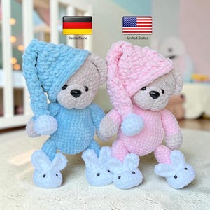 Pode incluir: Dois ursos de peluche, um azul-claro e outro rosa-claro, cada um com um gorro de dormir a condizer de cauda longa e chinelos brancos em forma de coelho. Os ursos têm rostos cinzentos, olhos e narizes pretos, feitos de fio macio e texturado.