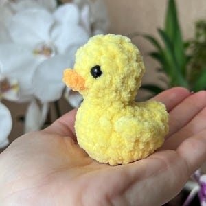 Puede incluir: Un peque&ntilde;o pato amarillo de peluche con pico naranja y ojos negros. El juguete hecho a mano es suave y esponjoso, perfecto para una colecci&oacute;n de juguetes infantiles. El pato est&aacute; sostenido en la mano de una persona.