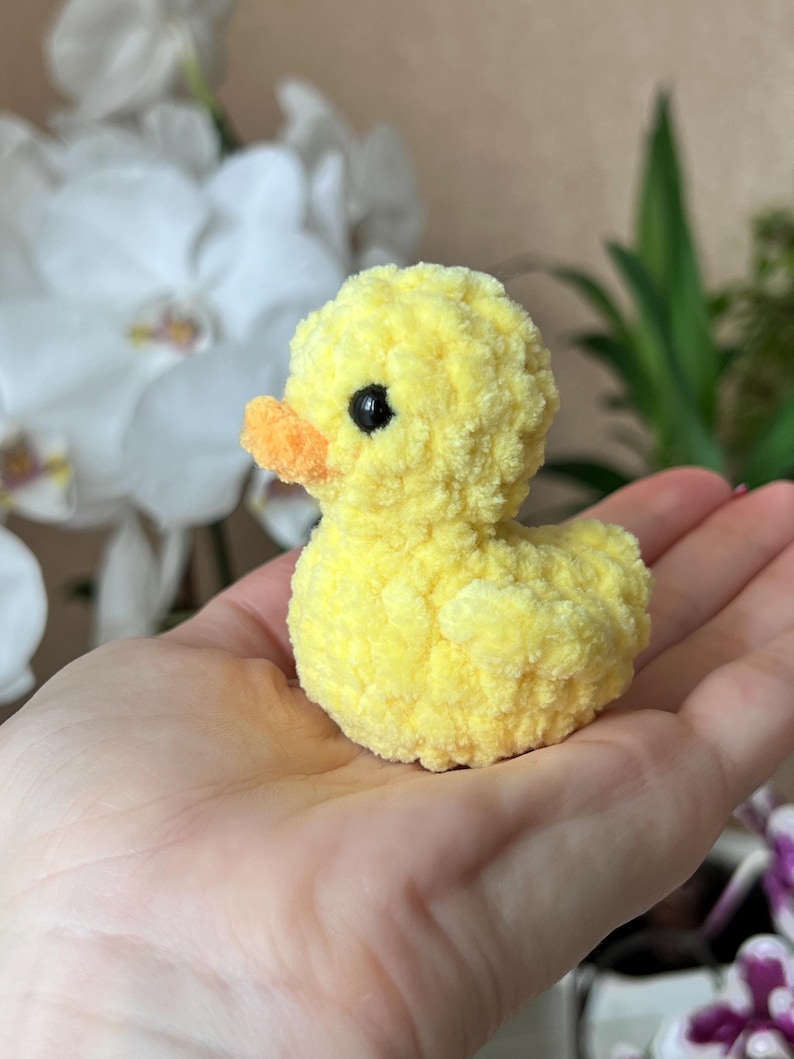 Puede incluir: Un peque&ntilde;o pato amarillo de peluche con pico naranja y ojos negros. El juguete hecho a mano es suave y esponjoso, perfecto para una colecci&oacute;n de juguetes infantiles. El pato est&aacute; sostenido en la mano de una persona.