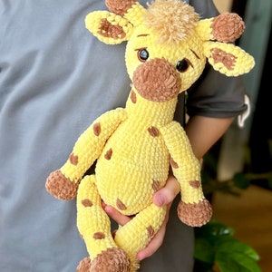 May include: A crocheted giraffe soft toy with brown spots and a brown nose. The giraffe is yellow and has a brown and white mane.