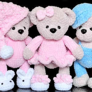 Könnte beinhalten: Drei handgefertigte Häkel-Teddybären aus weichem Plüschgarn. Der linke Bär trägt eine rosa Schlafmütze und weiße Hausschuhe. Der mittlere Bär hat eine rosa Schleife und ein rosa Kleid mit weißen Schuhen. Der rechte Bär trägt eine blaue Mütze und Latzhose.