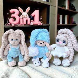 May include: Three plush crochet bunnies. The left bunny wears blue overalls. The center bunny wears a blue nightcap with a white pom-pom and matching slippers. The right bunny wears a white dress. Above them, a pink sign reads 3 in 1.