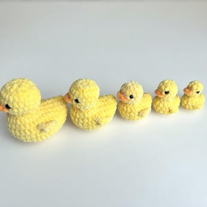 Puede incluir: Una familia de cinco patos amarillos de ganchillo de varios tama&ntilde;os. Los patos tienen picos naranjas y peque&ntilde;os ojos negros. El pato m&aacute;s grande est&aacute; a la izquierda, el m&aacute;s peque&ntilde;o a la derecha. Los patos est&aacute;n dispuestos en fila.