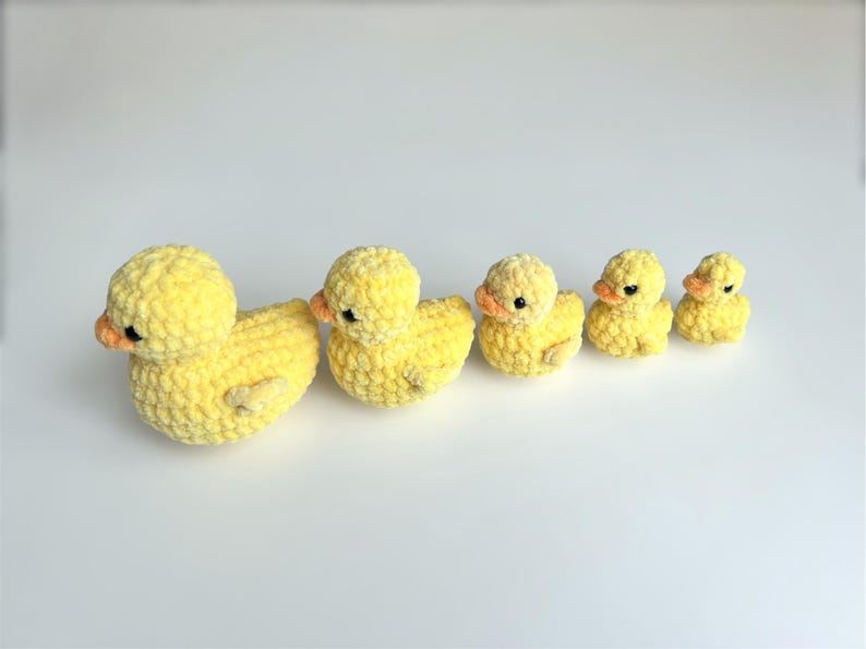 Puede incluir: Una familia de cinco patos amarillos de ganchillo de varios tama&ntilde;os. Los patos tienen picos naranjas y peque&ntilde;os ojos negros. El pato m&aacute;s grande est&aacute; a la izquierda, el m&aacute;s peque&ntilde;o a la derecha. Los patos est&aacute;n dispuestos en fila.