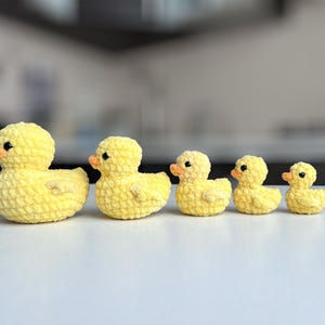 Puede incluir: Una fila de cinco patitos amarillos de ganchillo de diferentes tama&ntilde;os. Cada patito tiene un peque&ntilde;o pico naranja y ojos negros. Los patitos est&aacute;n dispuestos en l&iacute;nea, con el m&aacute;s grande a la izquierda y el m&aacute;s peque&ntilde;o a la derecha.