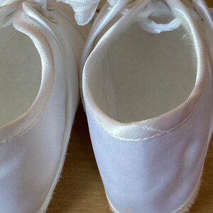 May include: A pair of white satin shoes with a lace-up closure. The shoes are new and have a clean, simple design.