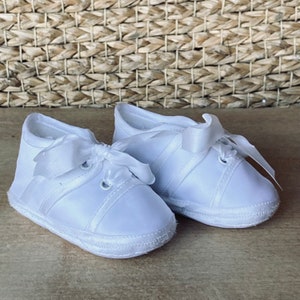 May include: A pair of white satin baby shoes with a satin ribbon tied in a bow on each shoe.