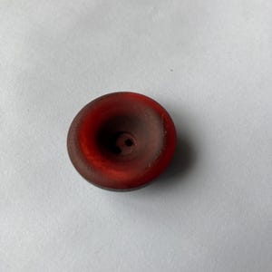 Può includere: Un bottone di plastica rosso scuro con due fori al centro.