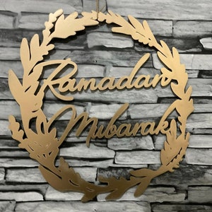 May include: A gold-coloured wooden wreath with the words "Ramadan Mubarak" written in a decorative script.