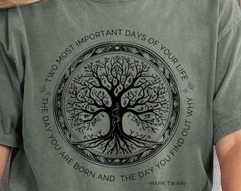 May include: Moss green t-shirt featuring a black tree of life design within a circular frame. The text reads "TWO MOST IMPORTANT DAYS OF YOUR LIFE: THE DAY YOU ARE BORN AND THE DAY YOU FIND OUT WHY" and "MARK TWAIN".