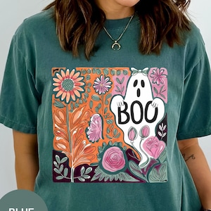May include: Blue spruce t-shirt with a colorful floral and ghost graphic. The graphic features a white ghost with the word "BOO" and is surrounded by orange, pink, and purple flowers and leaves. The shirt is a comfortable, casual style.