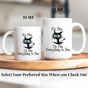 May include: Two white ceramic mugs with black cat illustrations and the text "It's Fine I'm Fine Everything Is Fine". The mugs are available in 11 oz and 15 oz sizes.