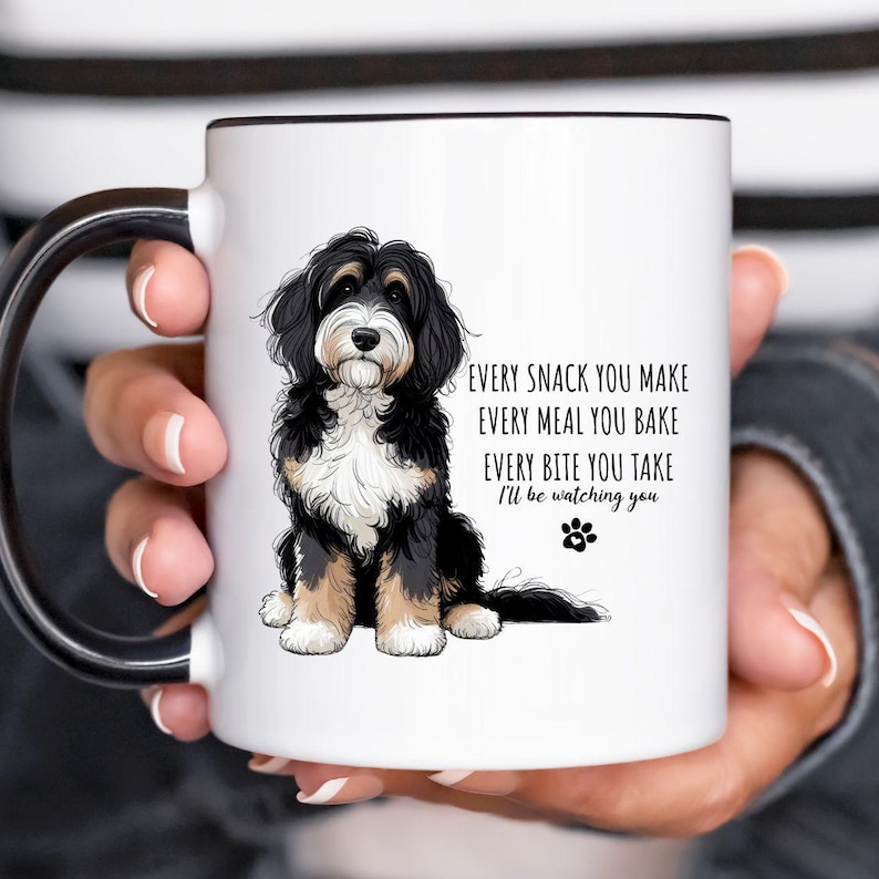 May include: White ceramic mug with a black handle and rim, featuring a black, brown, and white dog illustration. Text reads: "EVERY SNACK YOU MAKE, EVERY MEAL YOU BAKE, EVERY BITE YOU TAKE, I'll be watching you."