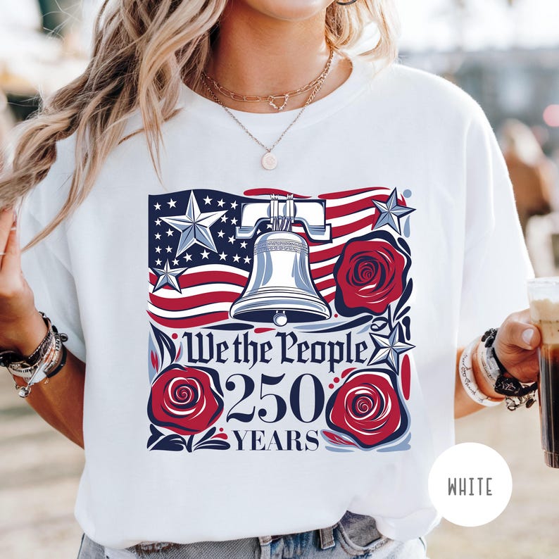 May include: White t-shirt with a patriotic design. The design includes the Liberty Bell, red roses, stars, and a stylized American flag. The text reads "We the People 250 Years."