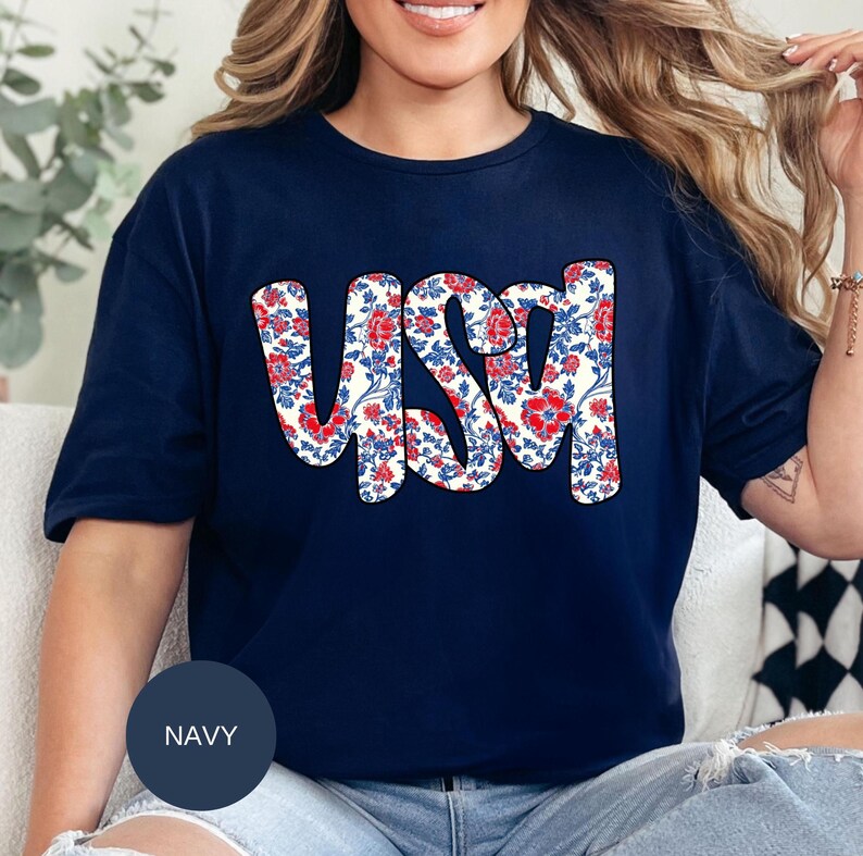 May include: A navy blue t-shirt with a white floral design that spells out "USA" in red and blue.