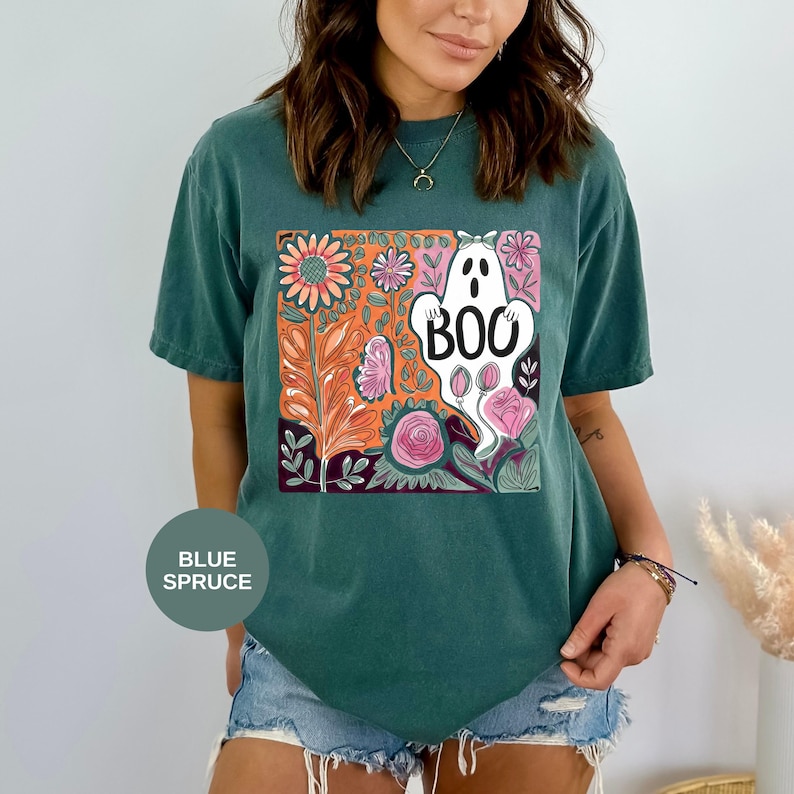 May include: Blue spruce t-shirt with a colorful floral and ghost graphic. The graphic features a white ghost with the word "BOO" and is surrounded by orange, pink, and purple flowers and leaves. The shirt is a comfortable, casual style.