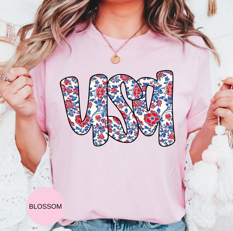 May include: A pink t-shirt with a floral pattern spelling out "USA" in a bold, white outline.