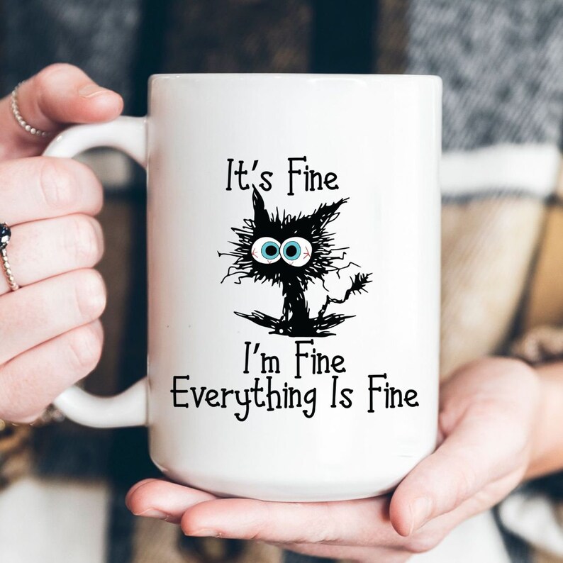 May include: White ceramic mug with a black cat illustration and the text "It's Fine. I'm Fine. Everything Is Fine."