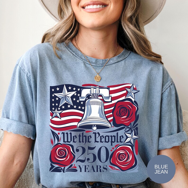 May include: Pale blue t-shirt with a patriotic design. The graphic features the Liberty Bell, American flag, stars, and roses. The text reads "We the People 250 Years."