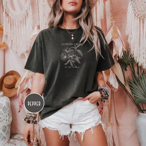 May include: Dark gray t-shirt with the text "FLOWERS GROW in the valley" and a floral graphic. The shirt is worn with white shorts. The word "PEPPER" is in a circle on the bottom left.