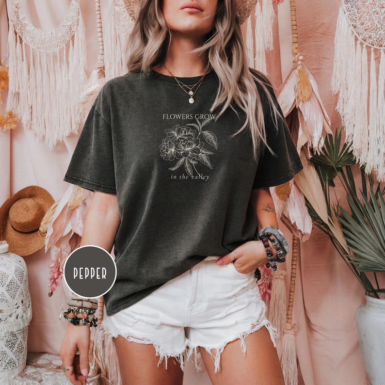 May include: Dark gray t-shirt with the text "FLOWERS GROW in the valley" and a floral graphic. The shirt is worn with white shorts. The word "PEPPER" is in a circle on the bottom left.