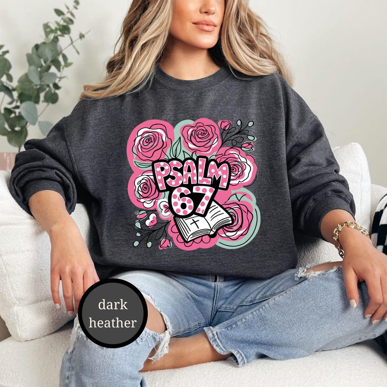 May include: Dark heather gray sweatshirt featuring a floral design with pink roses and the text "PSALM 67". The design includes an open book with a cross. The sweatshirt is a comfortable, casual style.
