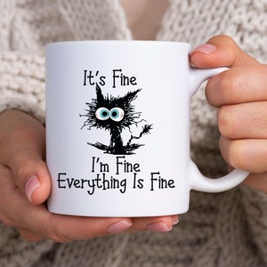 May include: White ceramic mug with a black cat illustration and the text "It's Fine I'm Fine Everything Is Fine".