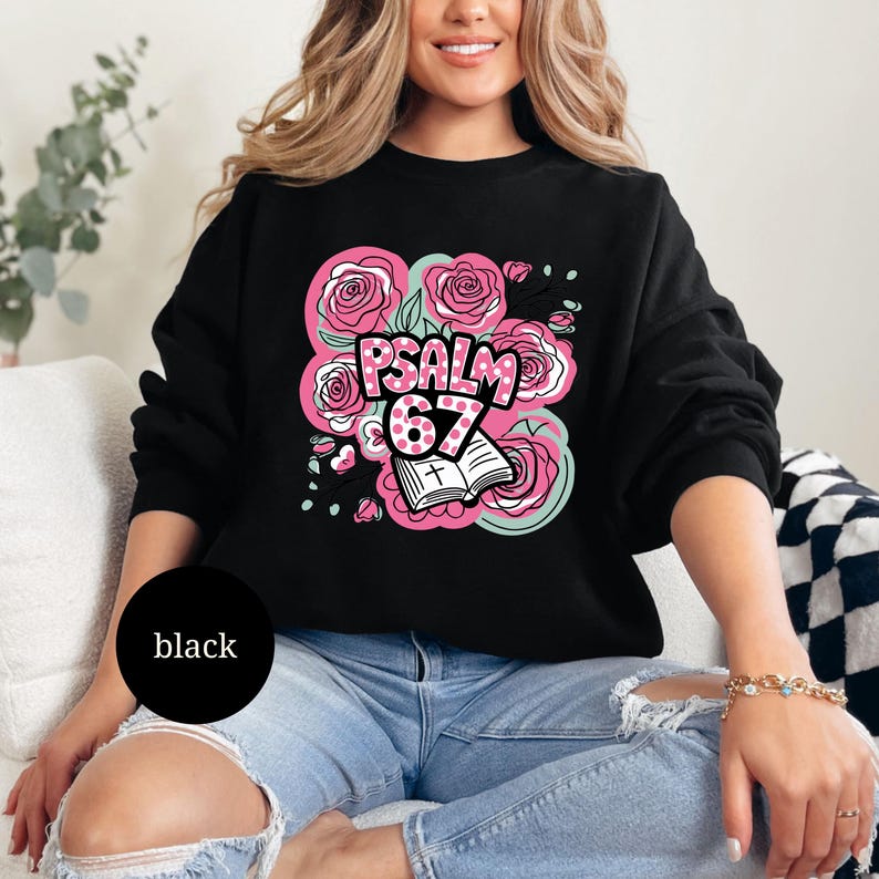 May include: Black sweatshirt with a floral design featuring pink roses, mint green accents, and the text "PSALM 67". An open book with a cross is also part of the design. The sweatshirt is a casual style.
