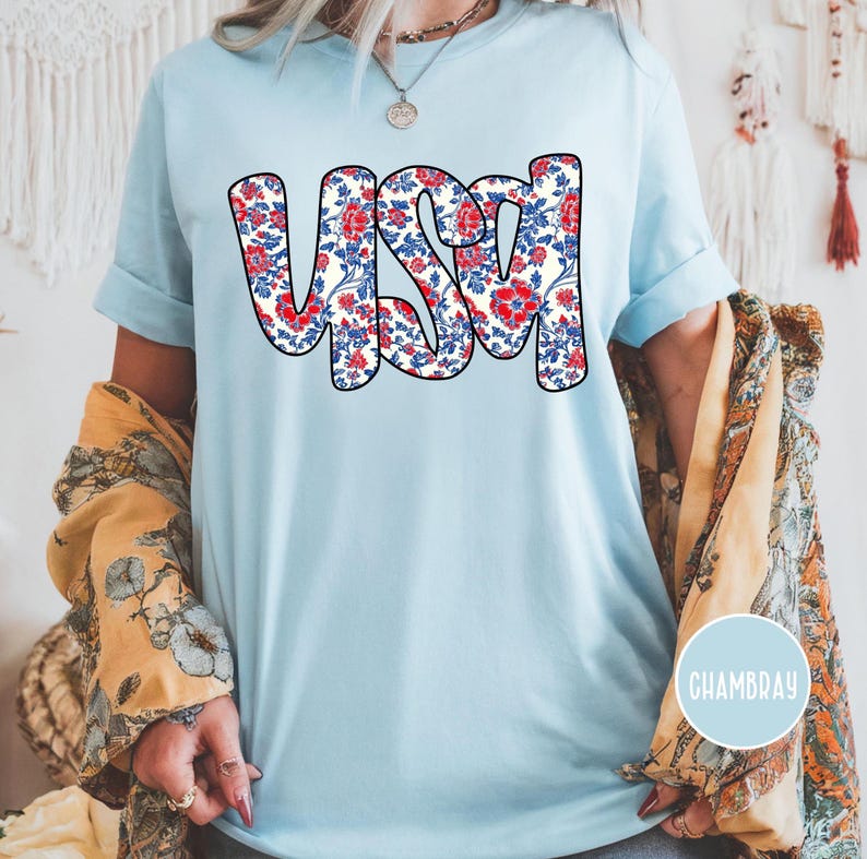 May include: A light blue t-shirt with a floral print design that spells out "USA". The shirt is made of a soft, comfortable chambray fabric.