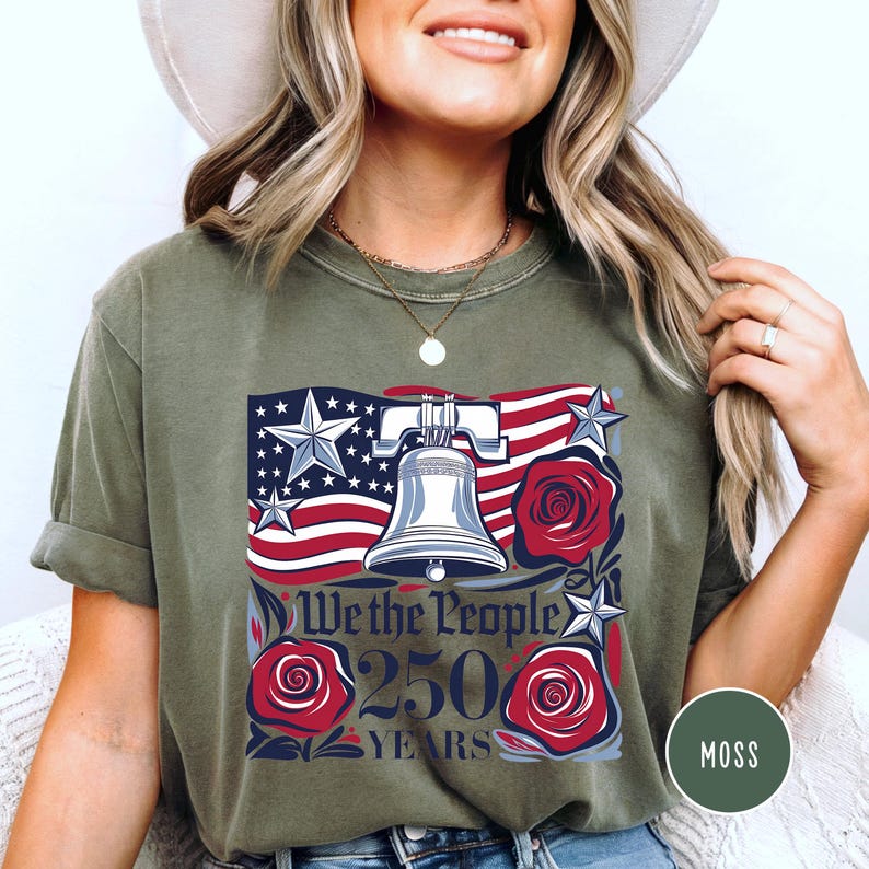 May include: Olive green t-shirt with a patriotic design. The design features the American flag, the Liberty Bell, and red roses, with the text "We the People 250 Years." The shirt is a casual style, suitable for everyday wear.