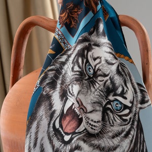 Puede incluir: Un pañuelo de seda con estampado azul y marrón drapeado sobre un jarrón de terracota, con un tigre blanco de ojos azules impreso en él.