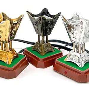 May include: Three electric incense burners with ornate designs. The burners are gold, silver, and black and are on brown bases with green inserts.
