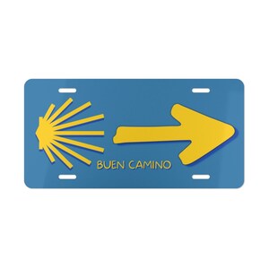 May include: A blue and yellow license plate with a yellow scallop shell and arrow pointing to the right. The text "BUEN CAMINO" is printed in yellow below the arrow.