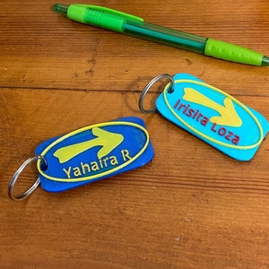 May include: Two blue keychains with yellow arrows and white text. The keychain on the left says "Yahaira R" and the keychain on the right says "Irisira Loza".