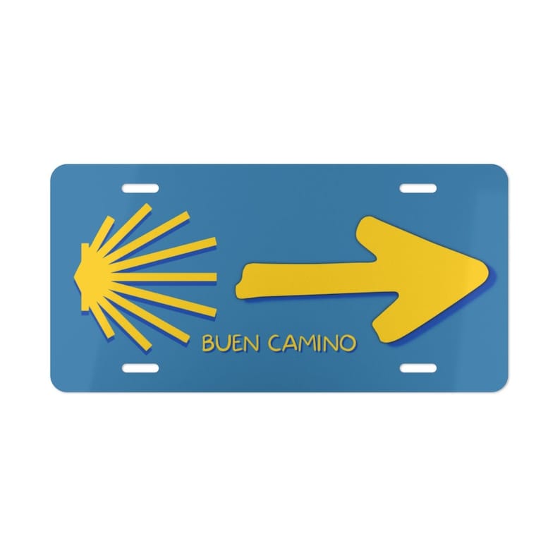 May include: A blue and yellow license plate with a yellow scallop shell and arrow pointing to the right. The text "BUEN CAMINO" is printed in yellow below the arrow.