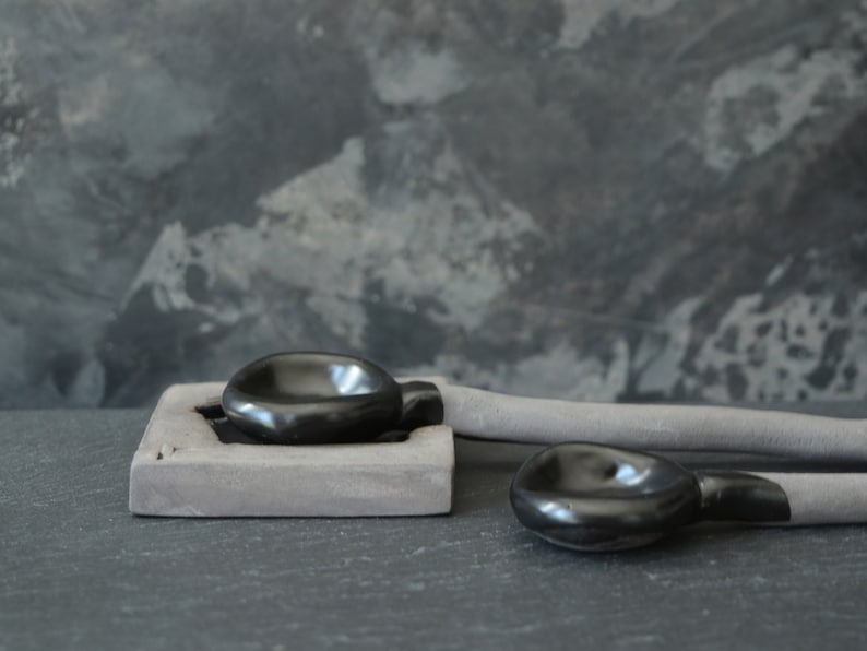 May include: Two black ceramic bowls, one on a gray rectangular base, the other on a gray ceramic handle. The bowls are smooth and glossy.