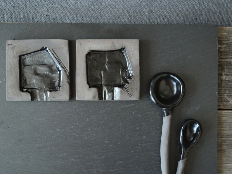 May include: Two black ceramic tiles with a raised design and two black ceramic spoons.