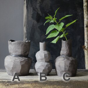 K&ouml;nnte beinhalten: Drei graue Keramikvasen in verschiedenen Formen und Gr&ouml;&szlig;en. Die Vase mit der Bezeichnung 'A' ist eine hohe, zylindrische Vase mit einer breiten &Ouml;ffnung. Die Vase mit der Bezeichnung 'B' ist eine runde, bauchige Vase mit einem schmalen Hals. Die Vase mit der Bezeichnung 'C' ist eine hohe, schlanke Vase mit einem schmalen Hals.