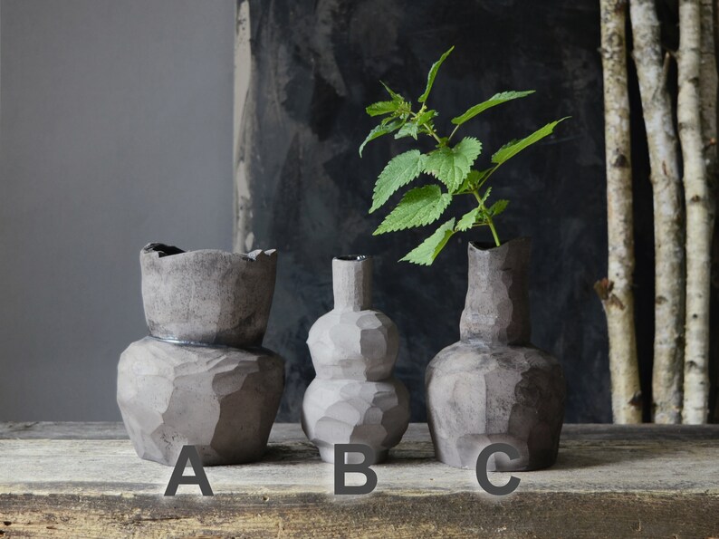 K&ouml;nnte beinhalten: Drei graue Keramikvasen in verschiedenen Formen und Gr&ouml;&szlig;en. Die Vase mit der Bezeichnung 'A' ist eine hohe, zylindrische Vase mit einer breiten &Ouml;ffnung. Die Vase mit der Bezeichnung 'B' ist eine runde, bauchige Vase mit einem schmalen Hals. Die Vase mit der Bezeichnung 'C' ist eine hohe, schlanke Vase mit einem schmalen Hals.