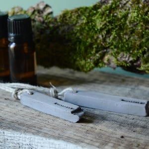 May include: Two small brown glass bottles with labels and a white string attached to two gray concrete rectangular diffuser pendants.