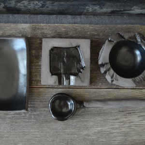 May include: A set of black ceramic kitchenware, including a rectangular plate, a small bowl, a spoon, and a square dish with a carved design.