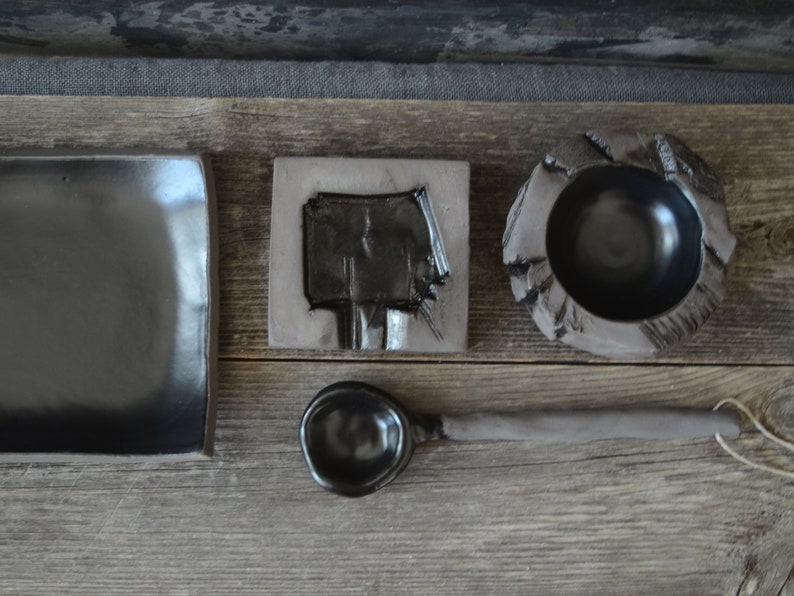 May include: A set of black ceramic kitchenware, including a rectangular plate, a small bowl, a spoon, and a square dish with a carved design.