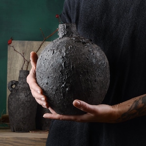 Puede incluir: Una persona sosteniendo un jarrón grande, redondo, de cerámica negra con una superficie texturizada.