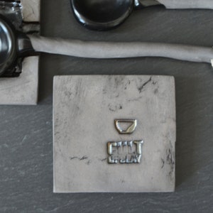 May include: A gray square tile with a small bowl imprint and the text "FILL IT UP, PLAY" in a silver metallic font.