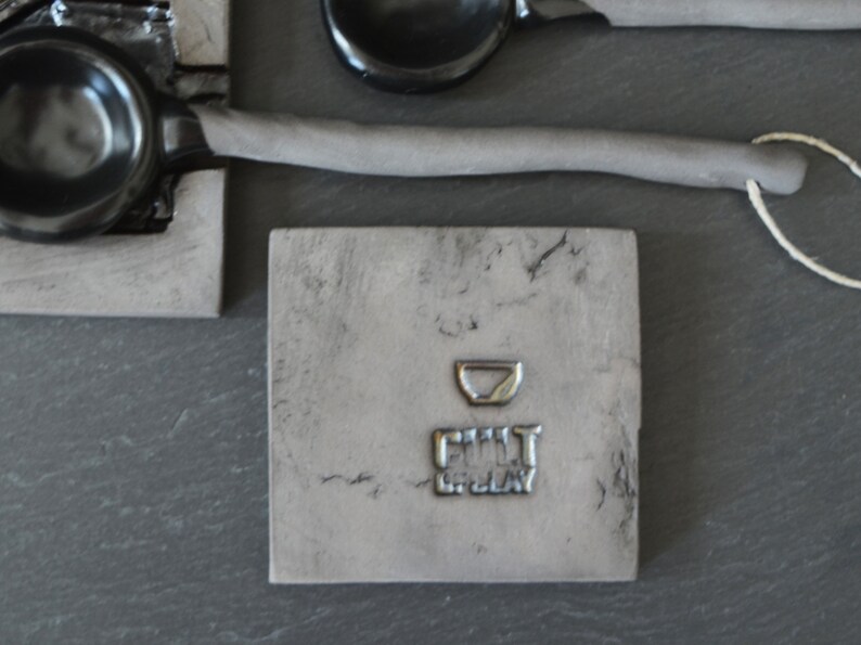 May include: A gray square tile with a small bowl imprint and the text "FILL IT UP, PLAY" in a silver metallic font.