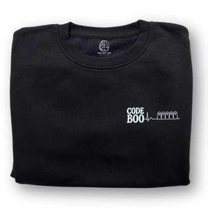 May include: A black crewneck sweatshirt featuring a white graphic on the chest. The graphic displays the text CODE BOO followed by a heartbeat line and four ghost icons. The inner neck label shows a brain icon and the text YOU GOT THIS.