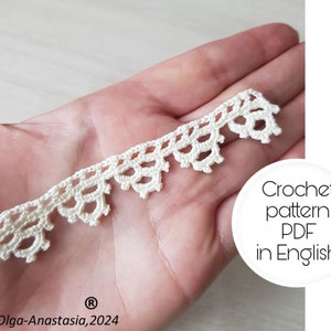 May include: A close-up of a cream-colored, crocheted lace trim. The trim features a scalloped edge design. Text on the image reads "Crochet pattern PDF in English" and "Olga-Anastasia, 2024".