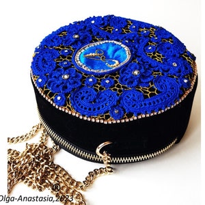 K&ouml;nnte beinhalten: Eine runde schwarze Samt-Handtasche mit einem blauen geh&auml;kelten Oberteil und einem goldenen Kettenriemen. Die Tasche hat einen Rei&szlig;verschluss und ist mit Strasssteinen verziert.